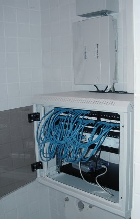 19" skriňa otvorená s prepojovacími káblikmi, nad ňou telefónna ústedňa